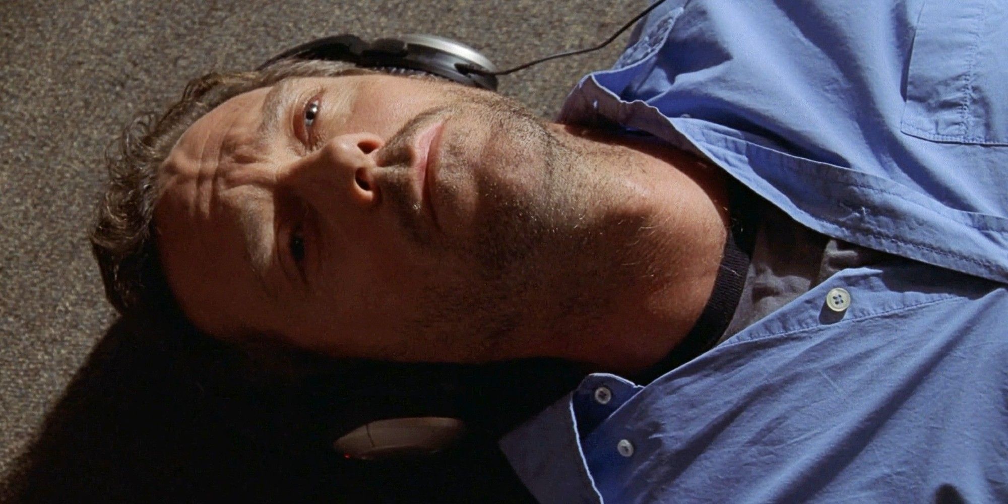 Hugh Laurie as Dr. Greg House lying on the floor of his office wearing headphones in House MD