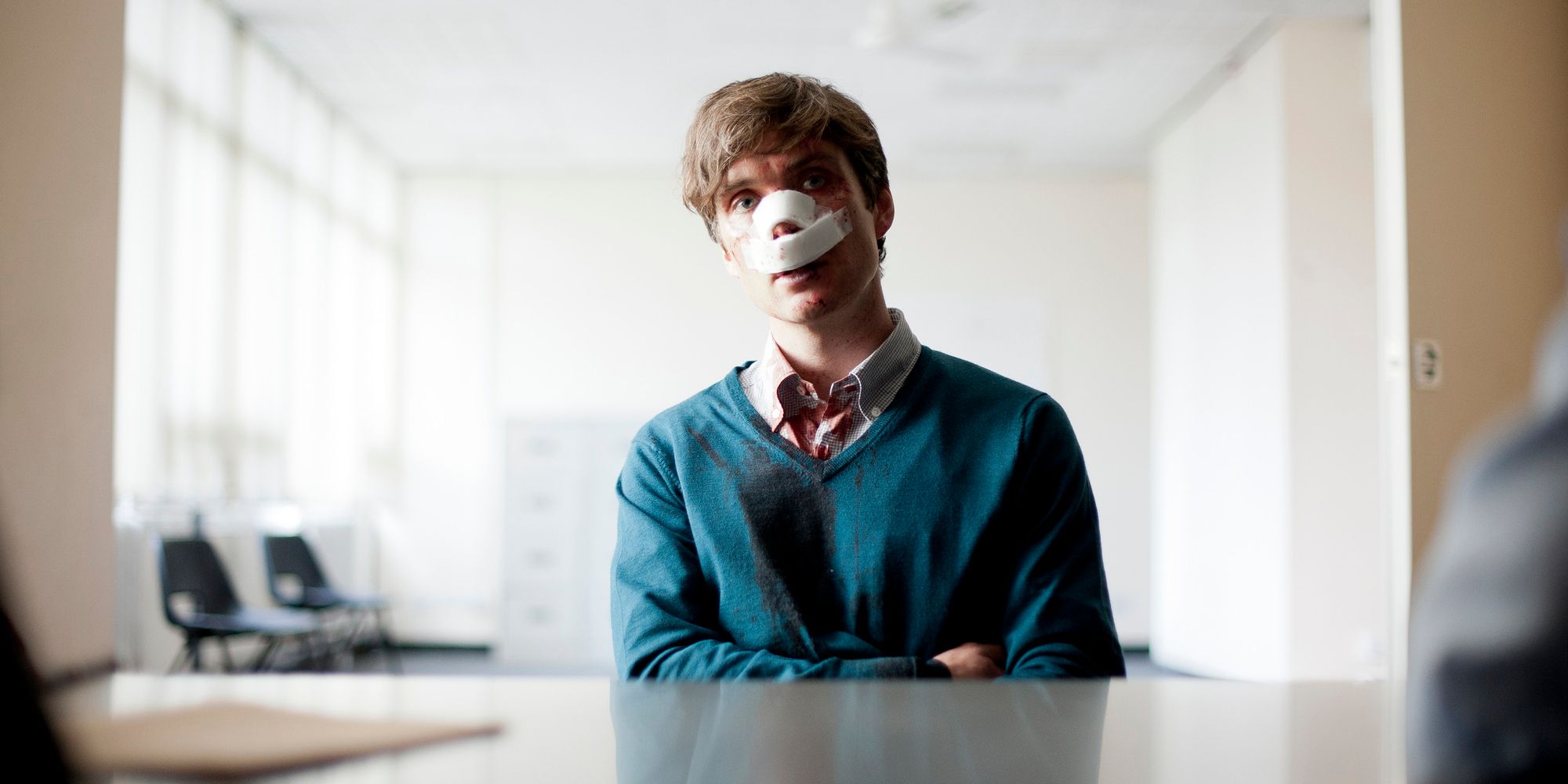 Cillian Murphy com o nariz enfaixado e os braços dobrados em quebra