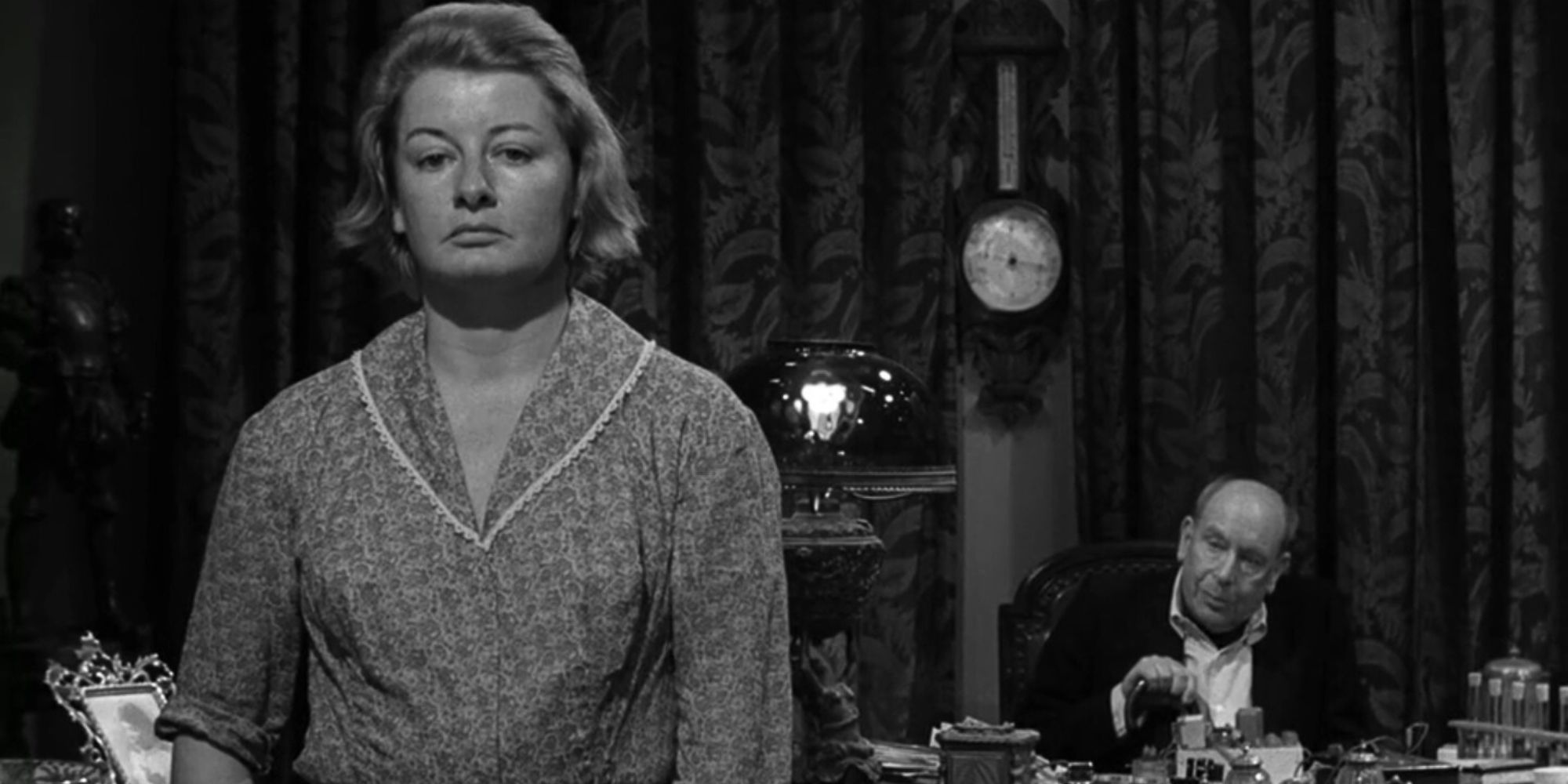 Cedric Hardwicke sitting at a desk behind Constance Ford in The Twilight Zone episode Uncle Simon