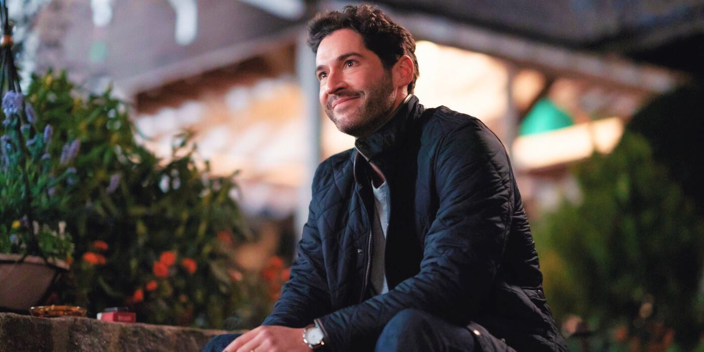 Tom Ellis as Oliver sitting down while looking up and smiling in Season 2 of Tell Me Lies.