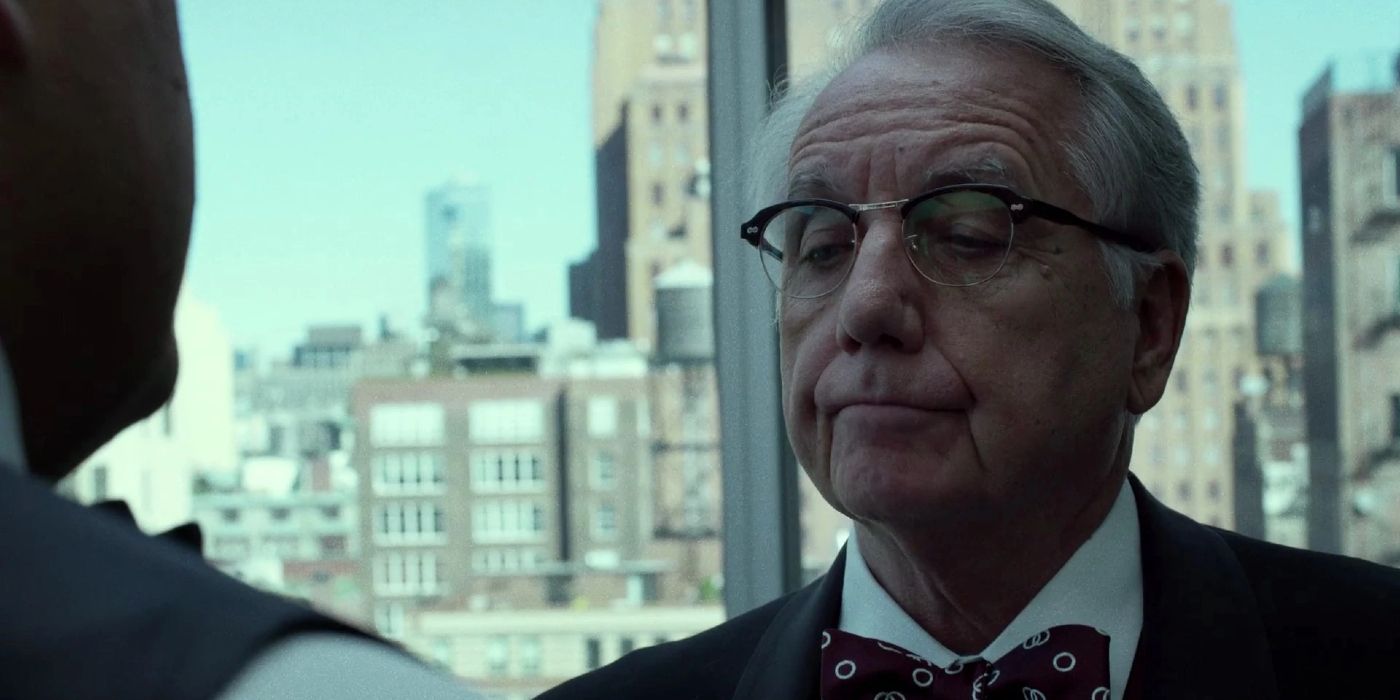 Bob Gunton as Leland Owlsley in a suit and bow tie in a tall office building talking to someone in Daredevil.