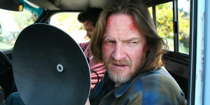 Two men sit in a vehicle and one holds up a small satellite dish in Terriers. 