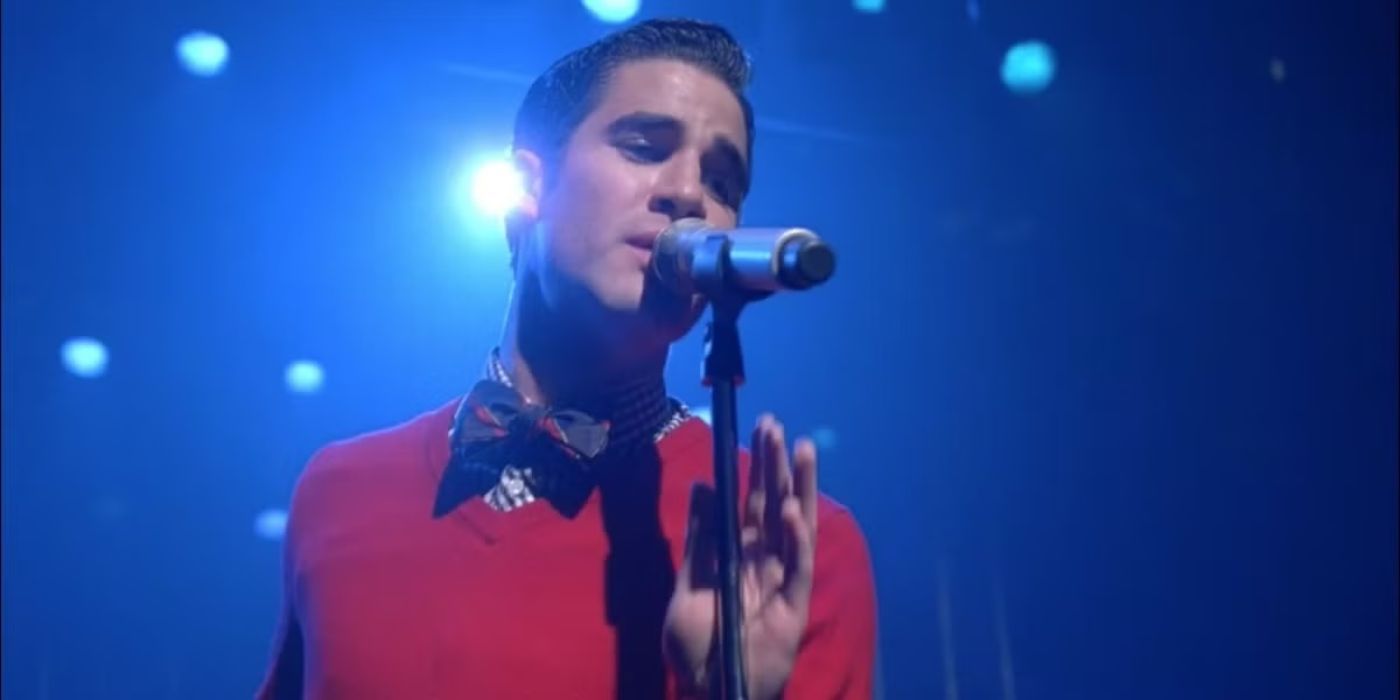 Darren Criss sings Cough Syrup into a microphone on stage in Glee Season 3.