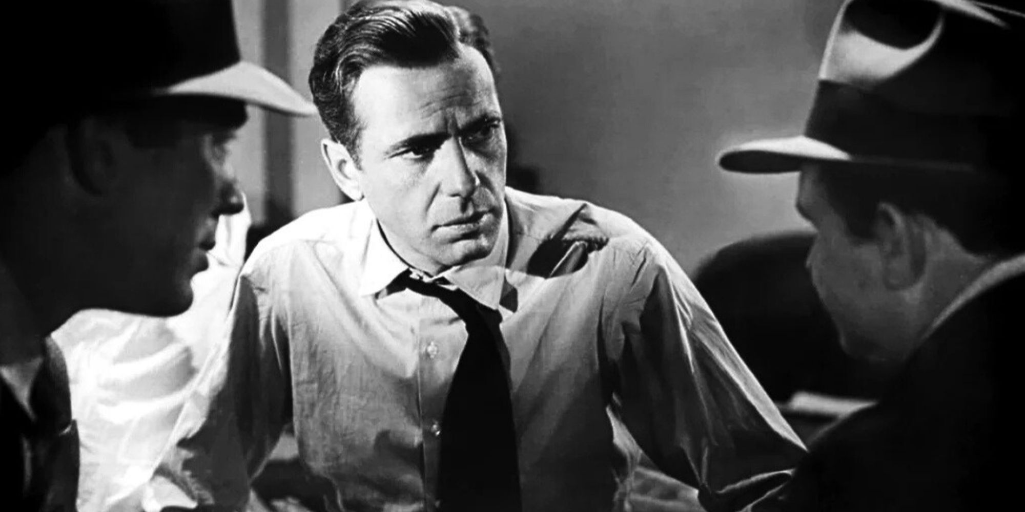 Humphrey Bogart as Sam Spade talking to two other men in The Maltese Falcon (1941).
