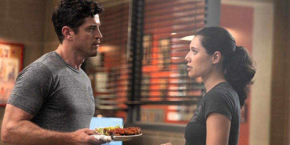 Jake Lockett as Sam Carver holding a plate of food, talking to Hanako Greensmith as Violet Mikami