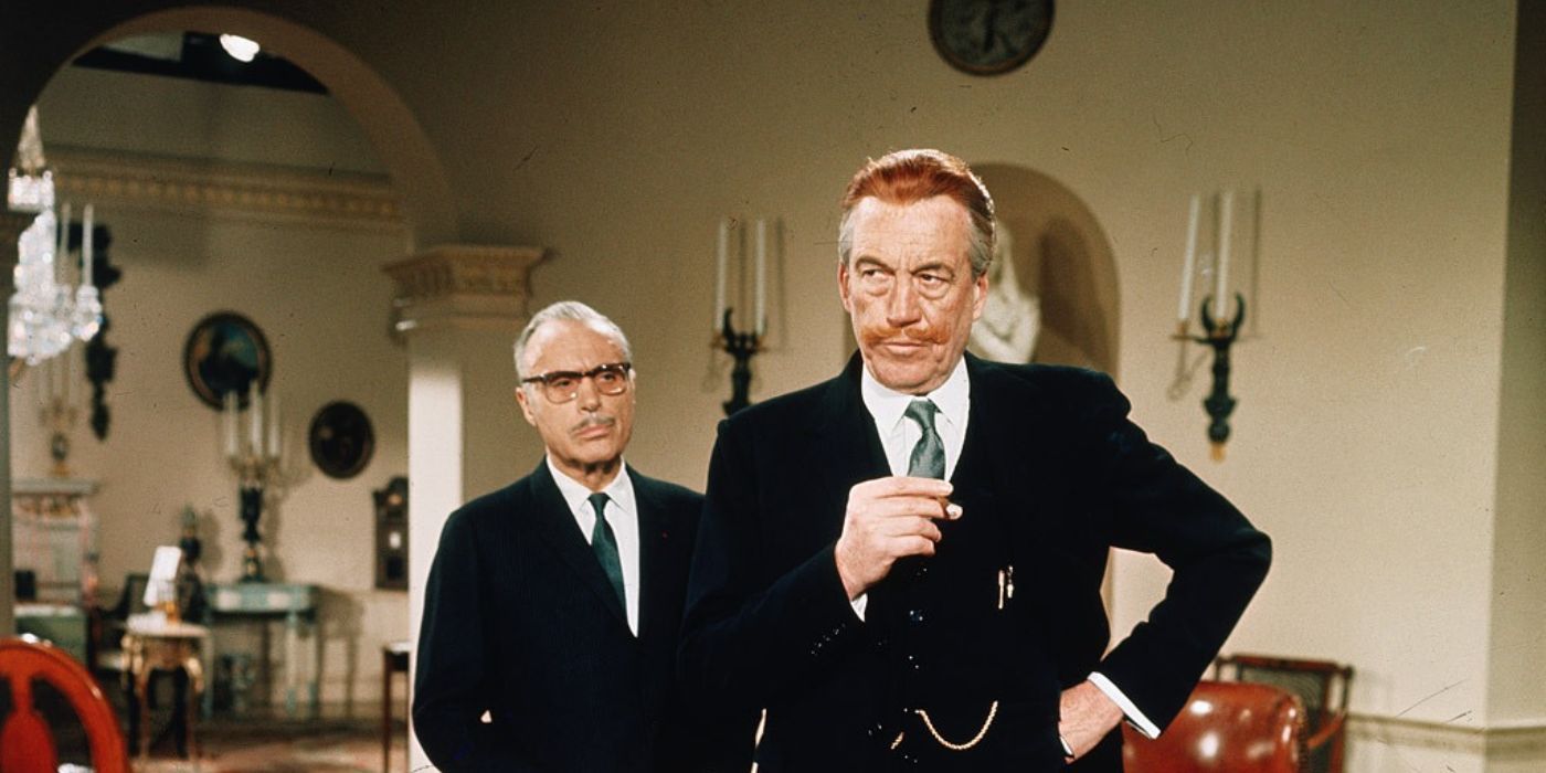 John Huston wears a suit and stands with his hand on his hip with another person behind in Casino Royale.