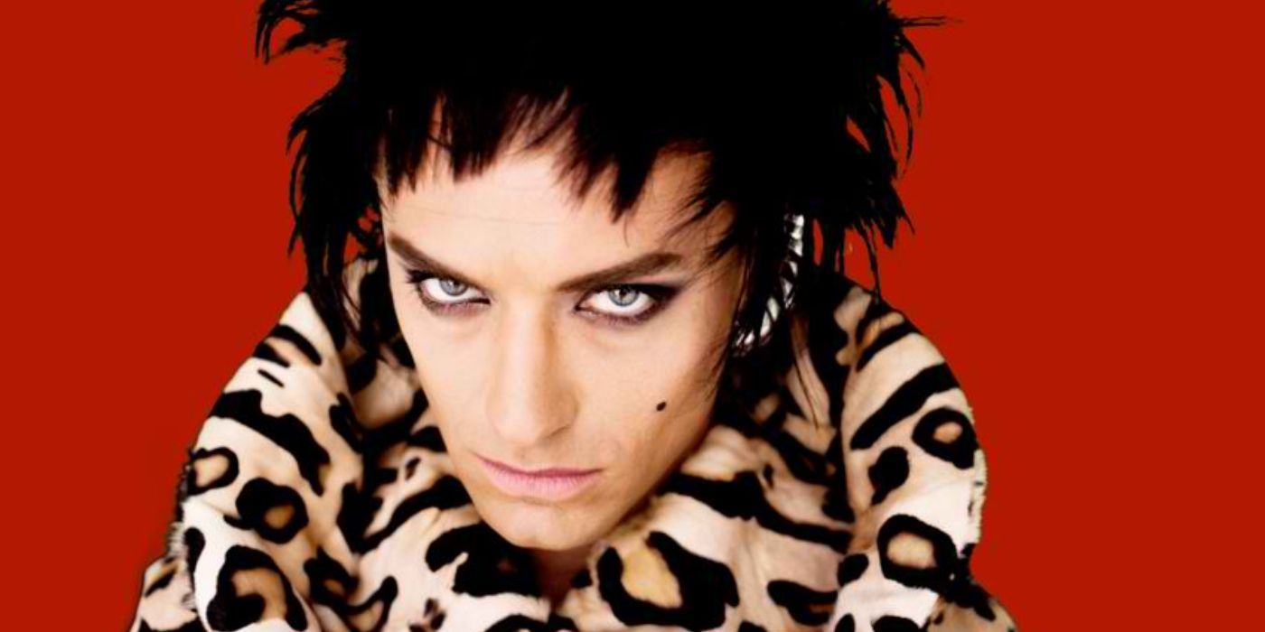 Jude Law as Minx wears a leopard print outfit and stares into the camera with a red background in Rage.