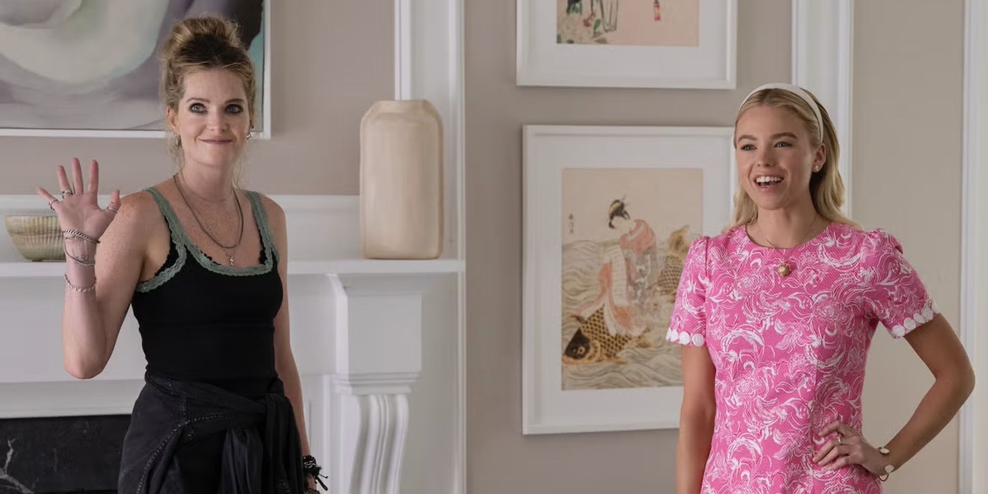 Meghann Fahy waving wearing a black tank top standing next to Milly Alcock smiling wearing a pink dress with one hand on her hip 