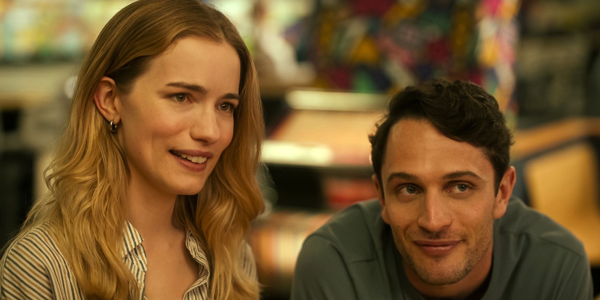 Willa Fitzgerald as Danny with a slight smile next to Colin Woodell as Phillips leaning on a counter in Pulse