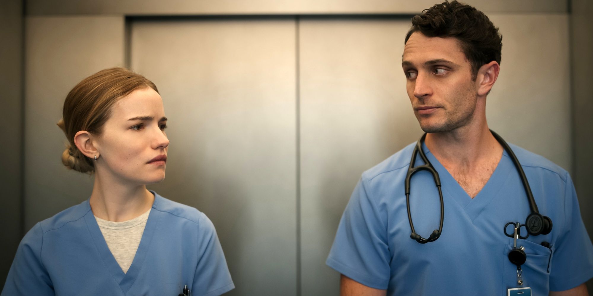 Willa Fitzgerald as Danny next to Colin Woodell as Phillips in their scrubs in an elevator in Pulse