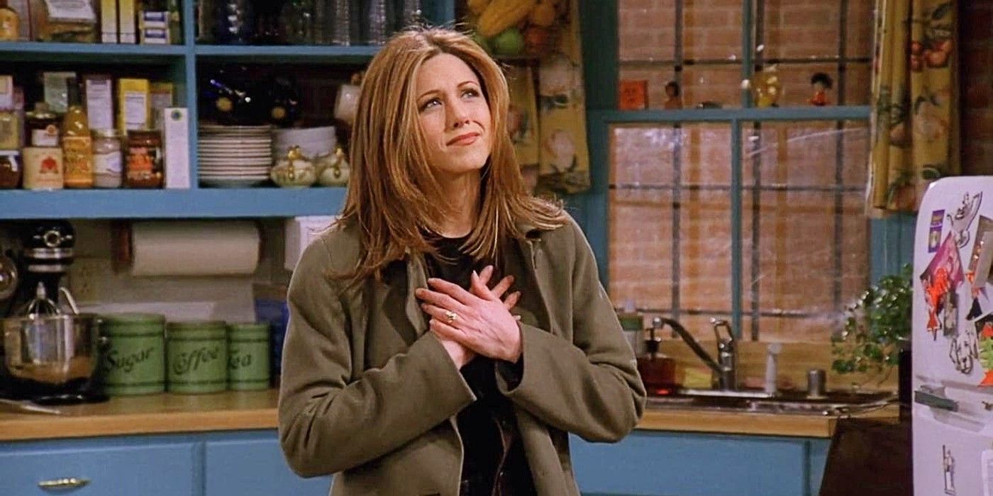 Rachel Green looks emotional, holding her hands to her chest, standing in an apartment in Friends Season 3.
