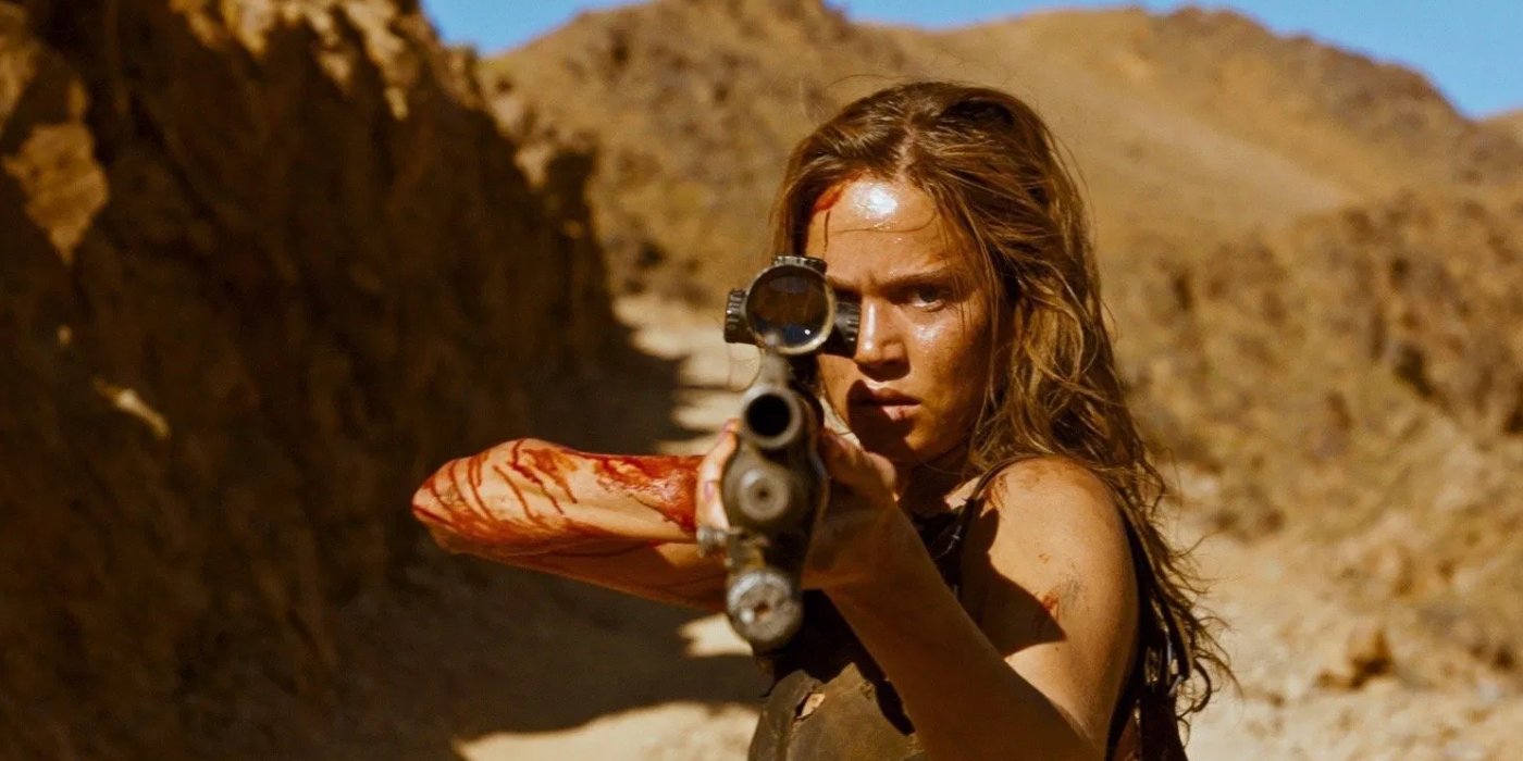 Matilda Lutz as Jen in Revenge points a shotgun at the camera.
