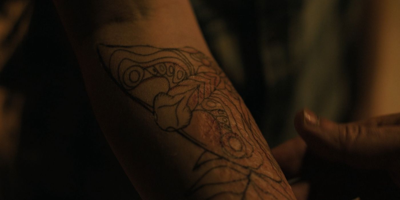 Um braço com uma tatuagem de uma mariposa com uma samambaia embaixo dela na última temporada da temporada 2