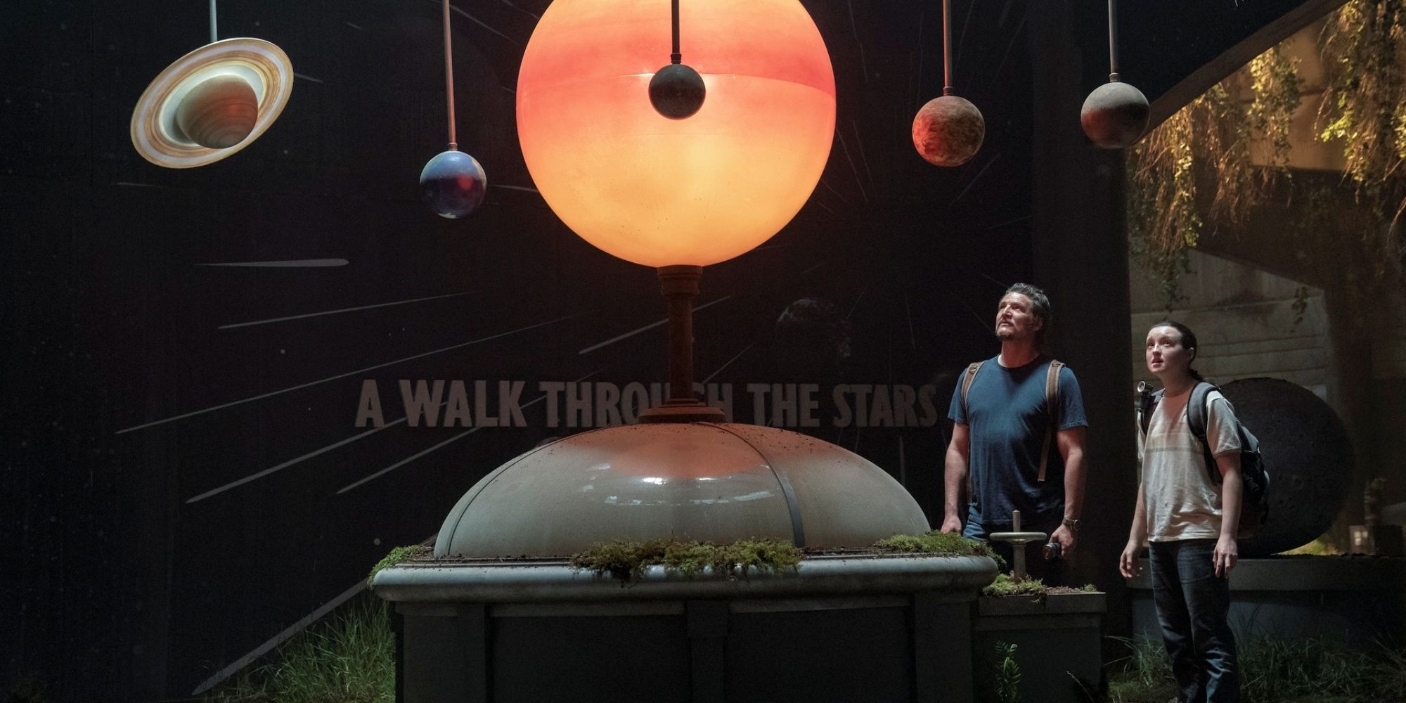 Bella Ramsey as Ellie with Pedro Pascal as Joel looking up at a display of planets in The Last of Us Season 2