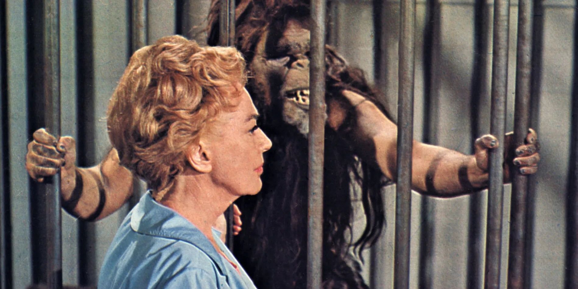 Joan Crawford stands outside a jail cell where a monster is imprisoned in a scene from Trog.