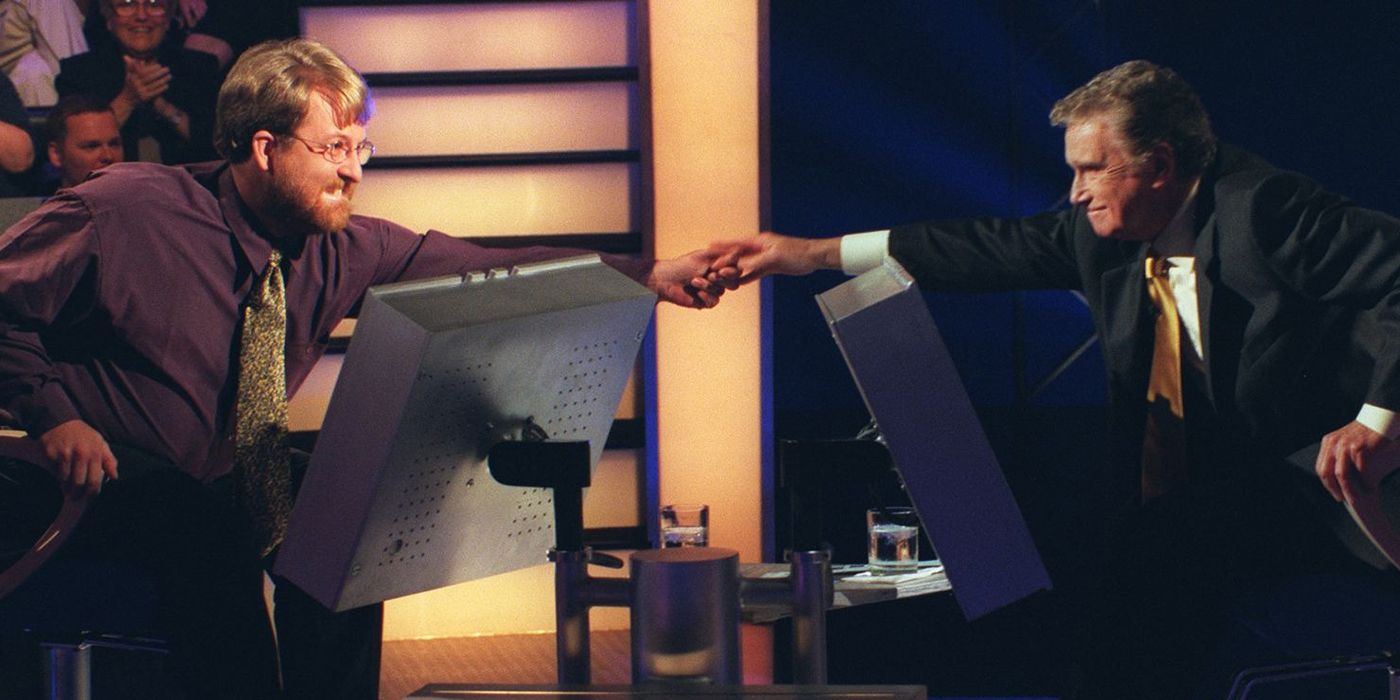 Regis reaching over to hold a male contestant's hand in Who Wants to be a Millionaire?
