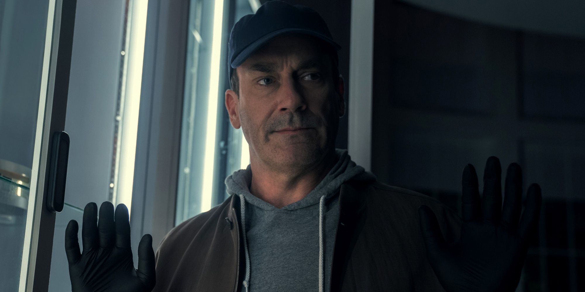 Jon Hamm as Coop in a baseball cap holding his hands up while wearing black gloves in Your Friends & Neighbors