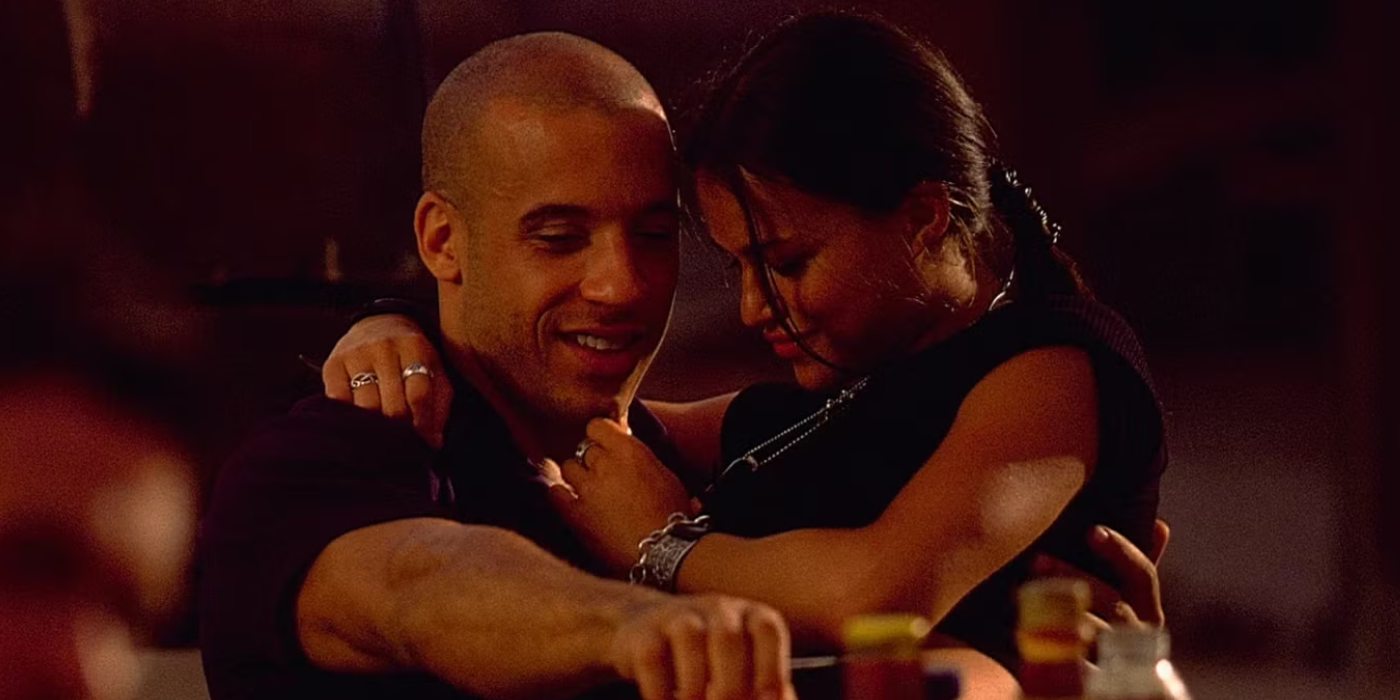 Letty sits in Dom's lap as they smile together in The Fast and The Furious, 2001.