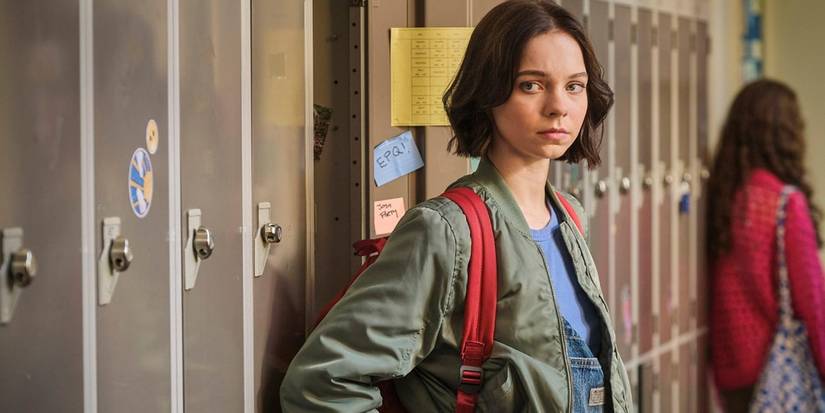Emma Myers looks down a school hallway while standing by lockers in A Good Girl's Guide to Murder. 