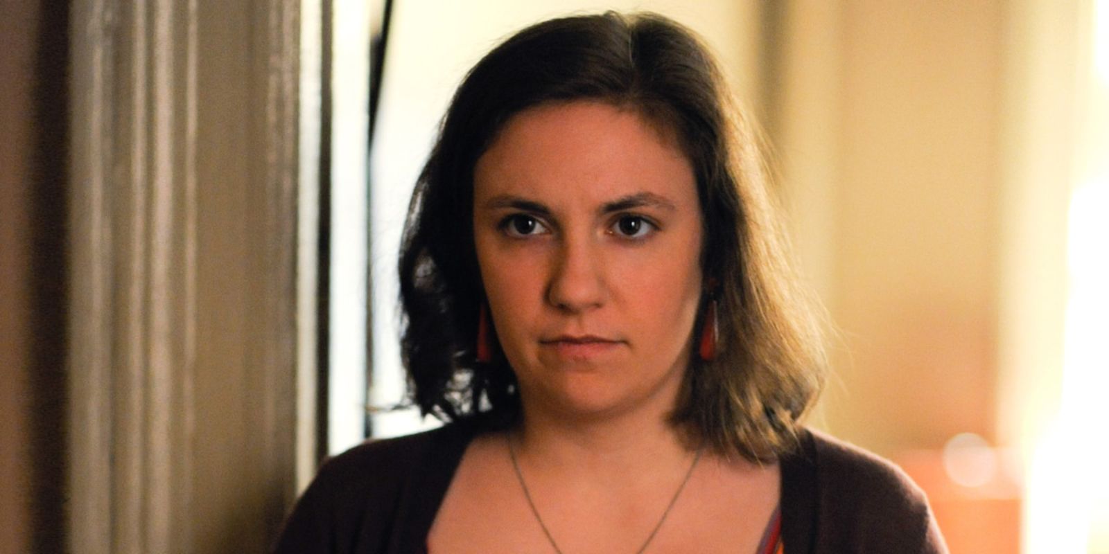 Hannah staring blankly ahead as she stands in a doorway in Girls.