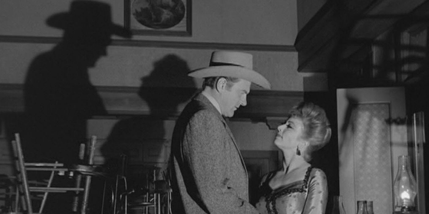 Maršals Metjū Dilons (Džeimss Arness) skatās uz Miss Kitty (Amanda Blake), kad viņu ēnas atlec uz sienas uz “Gunsmoke”