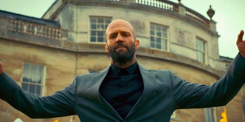 Jason Statham as Adam Clay with his hands up outside a mansion in The Beekeeper
