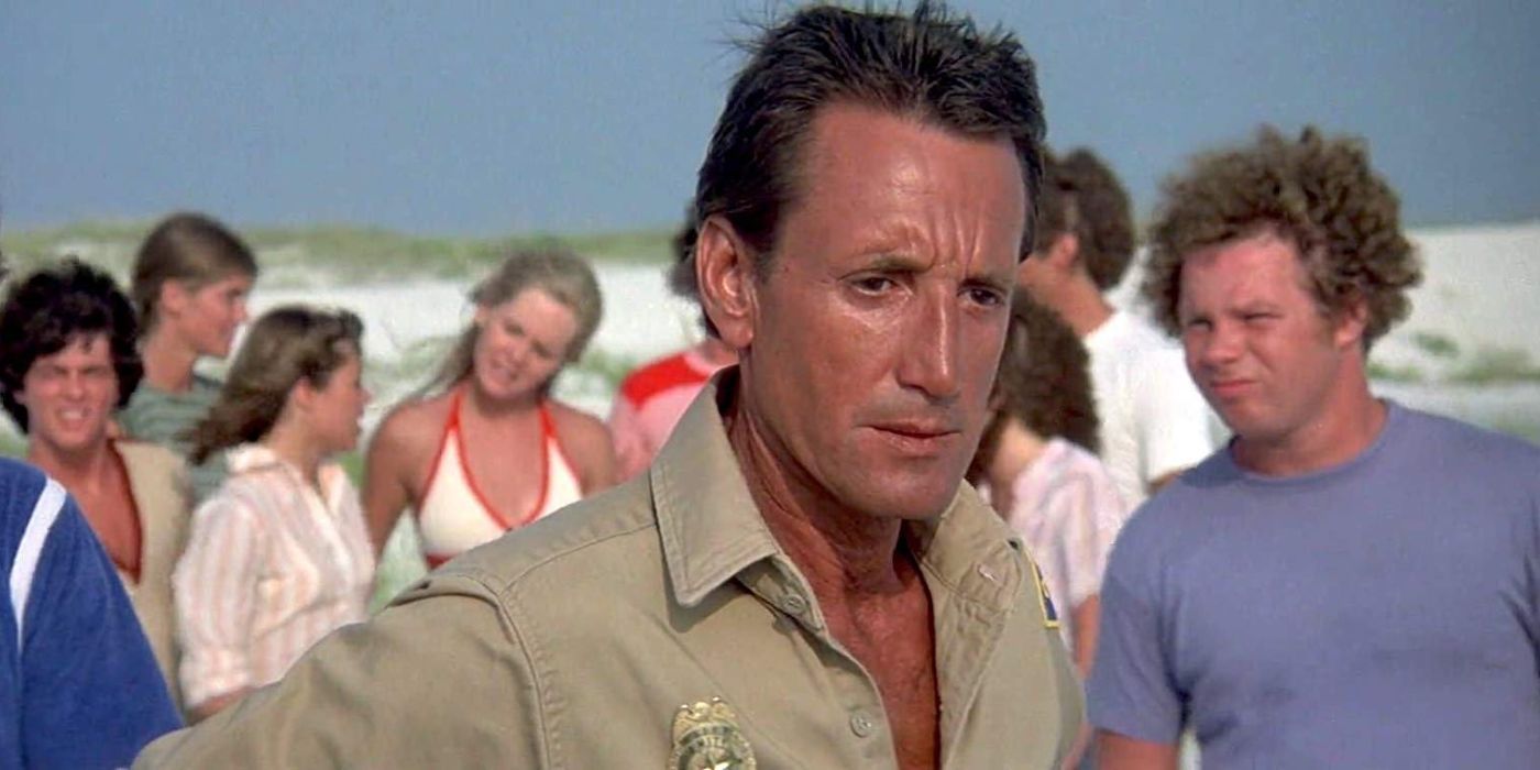 Roy Scheider como chefe Brody olhando para a água com os banhistas atrás dele em Jaws 2.