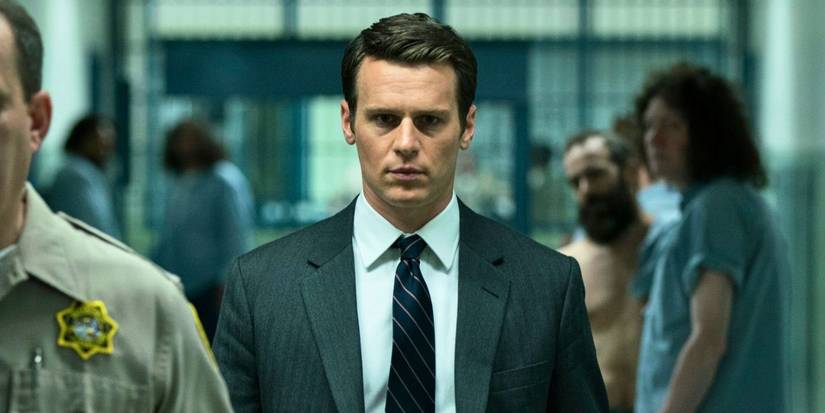 Jonathan Groff dans un costume et une cravate se promenant dans une prison dans Mindhunter.