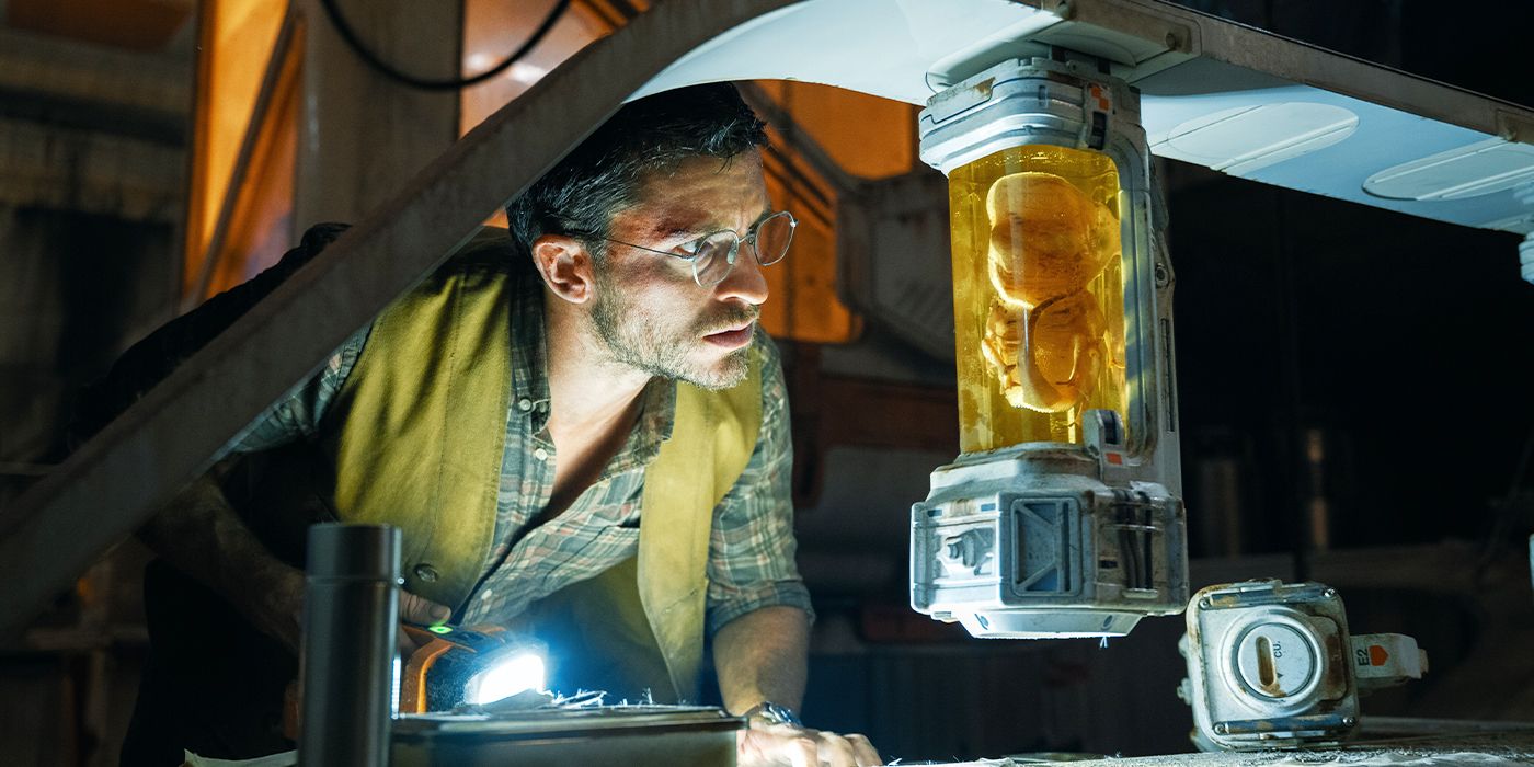 Jonathan Bailey looking into a large test tube holding a DNA sample in Jurassic World Rebirth