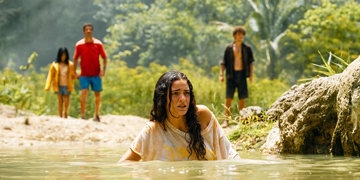 Teresa wading in a river with her family on the bank behind her in Jurassic World Rebirth
