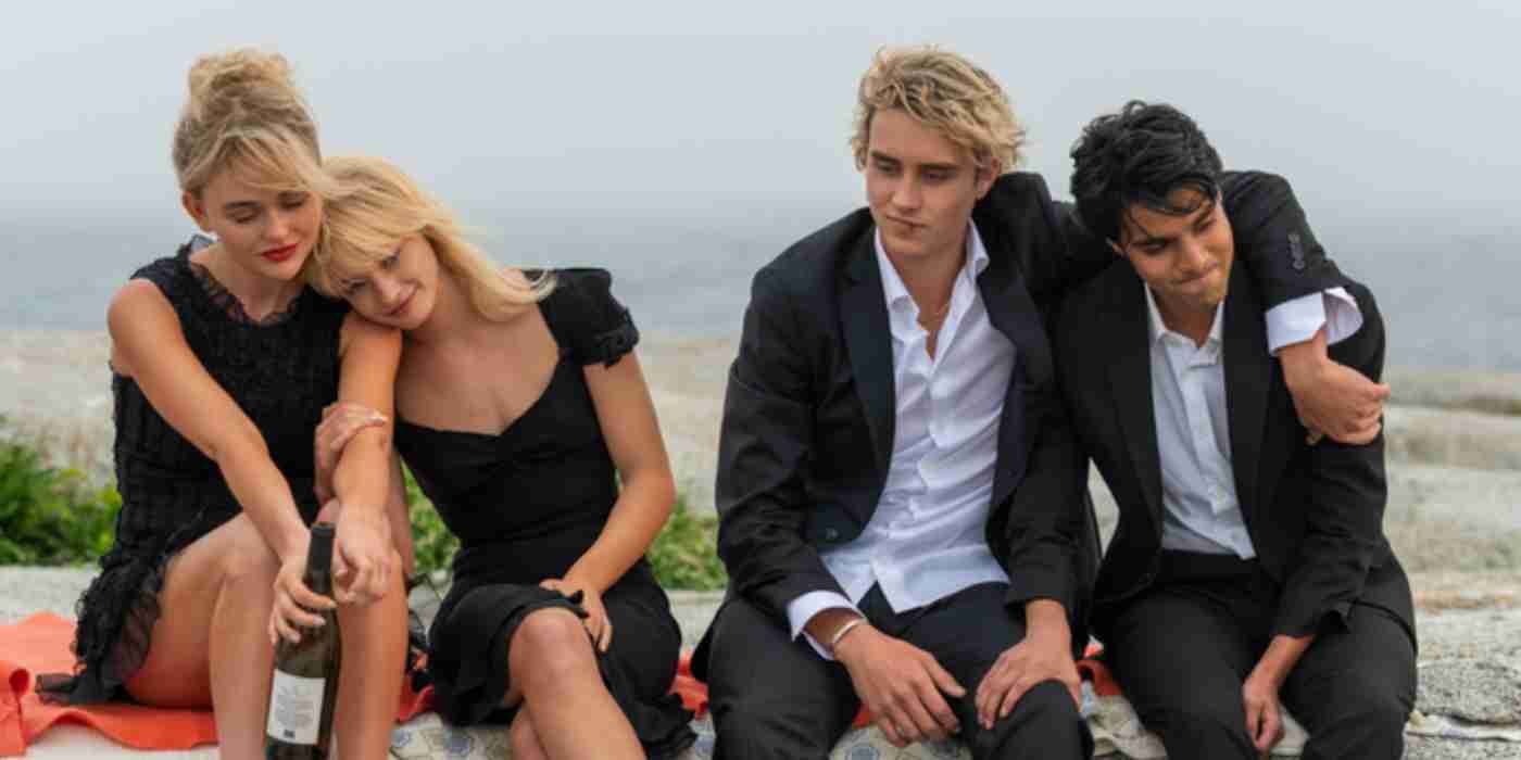 The four main characters of We Were Liars in formal attire sit on a beach and lean on each other.