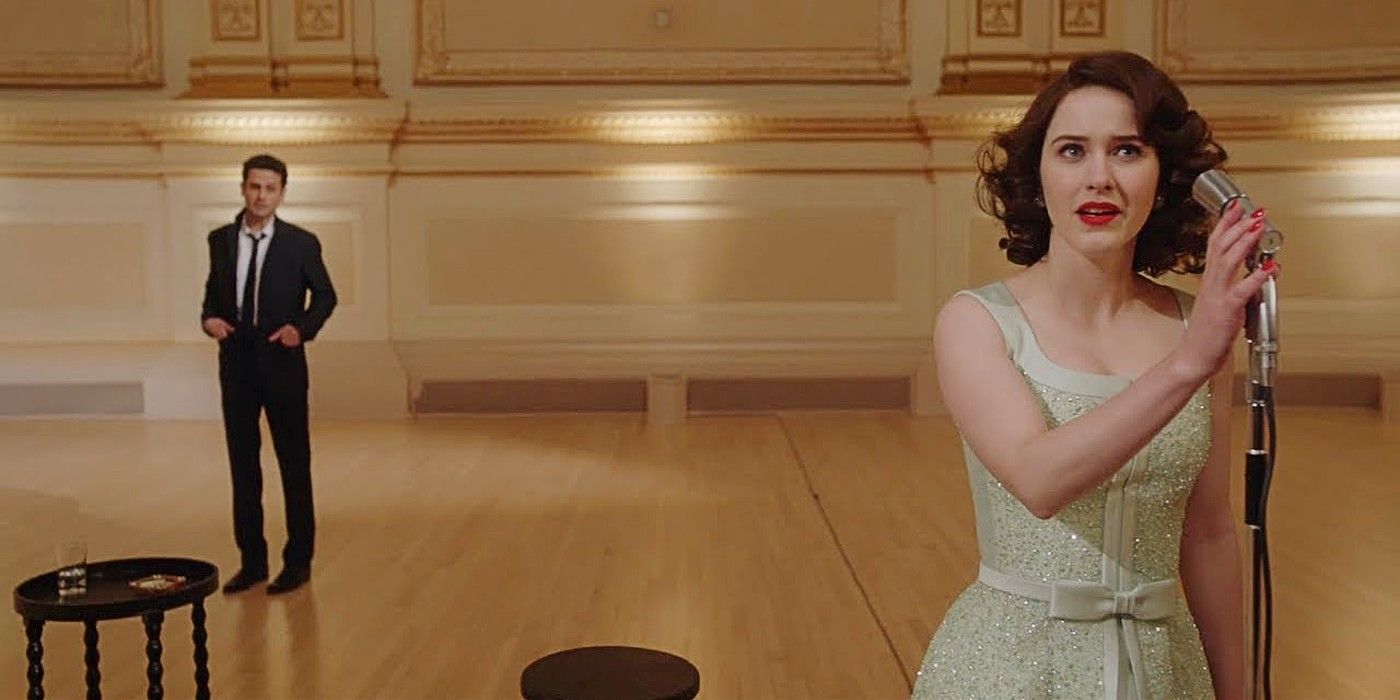 Midge standing at a microphone with Lenny in the background in The Marvelous Mrs. Maisel Season 4.