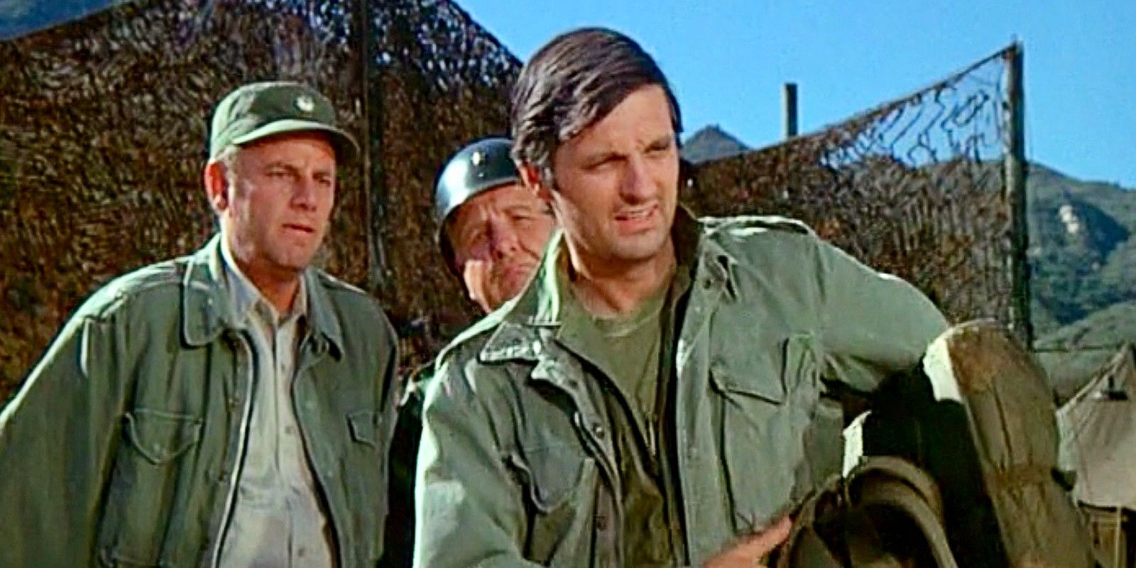 Alan Alda as Hawkeye looking at an object with others behind him in M*A*S*H Season 1.