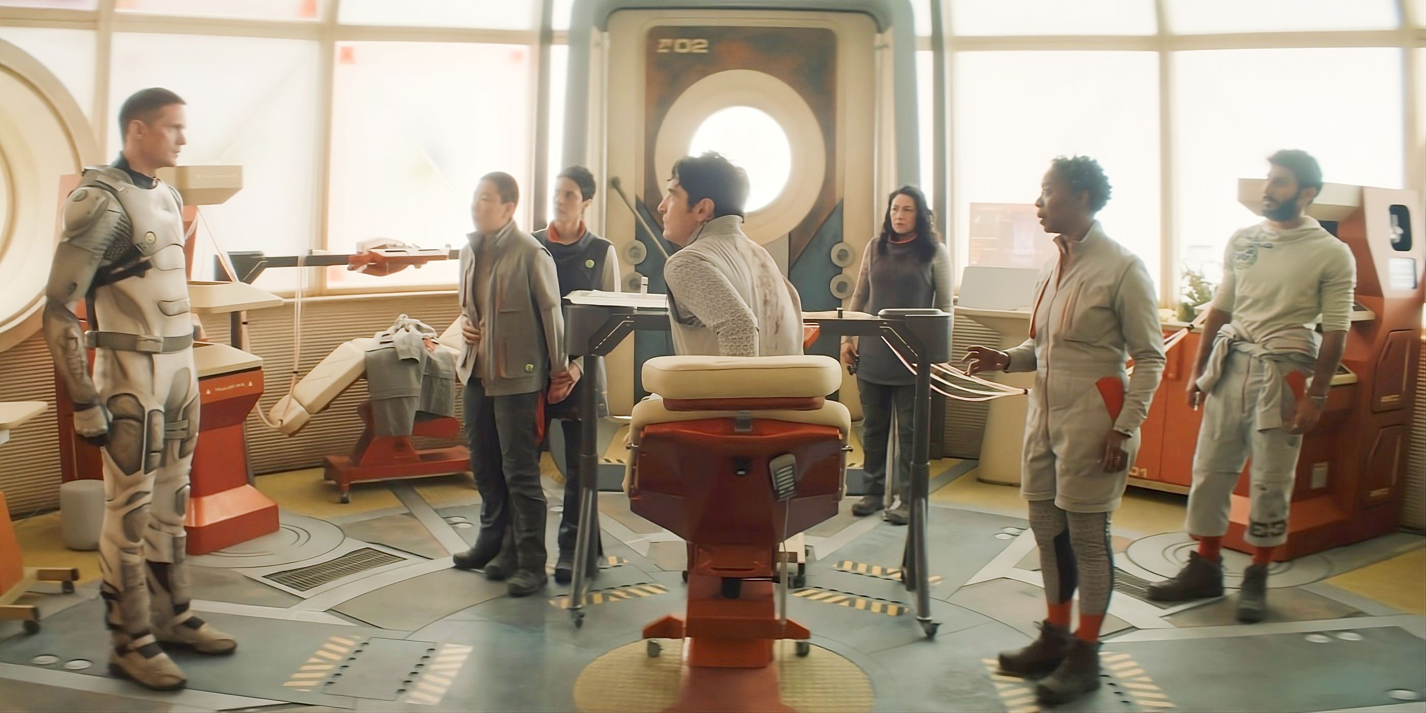 The Murderbot cast standing in the medbay, with the humans staring at Murderbot, in Episode 8