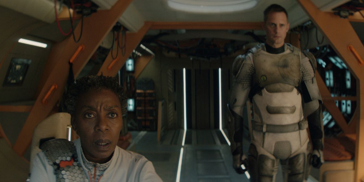 Mensah (Noma Dumezweni) sentado na cadeira piloto da Hopper com assassinato (Alexander Skarsgard) em pé atrás dela no episódio 5