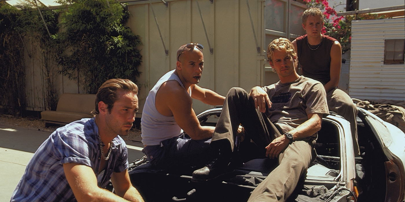 Four guys sit on a disassembled car in The Fast and the Furious, 2001.