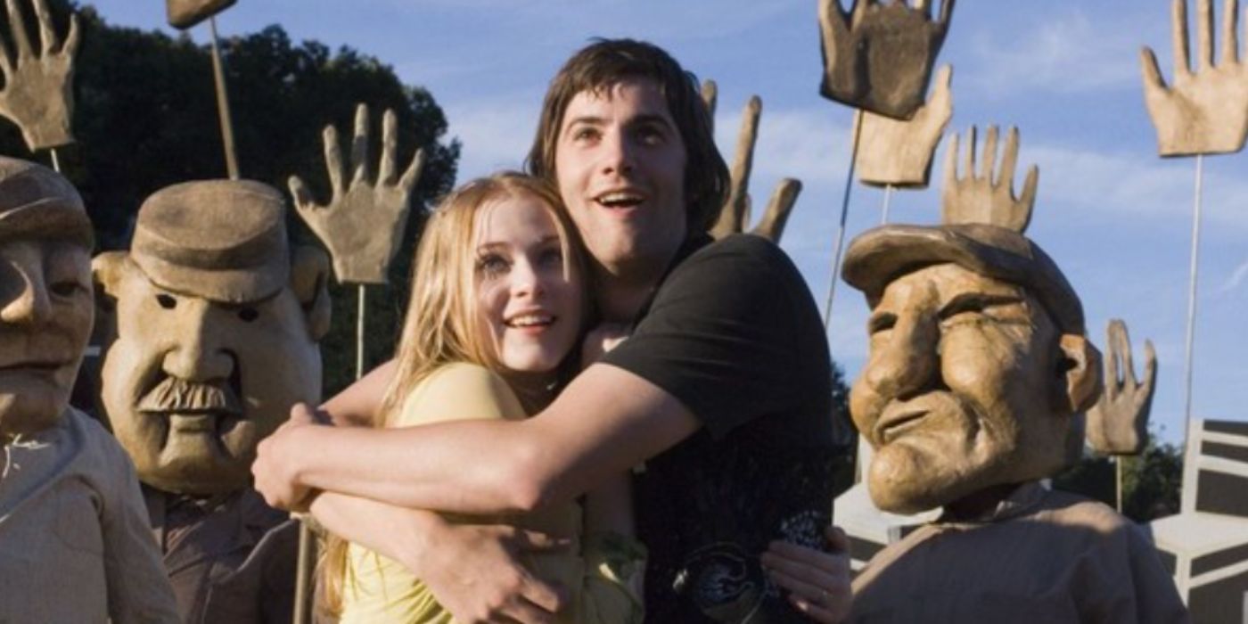 Evan Rachel Wood e Jim Sturgess como Lucy e Jude em pé e sorrindo em meio a argila de fora do lado de fora em 'do outro lado do universo'