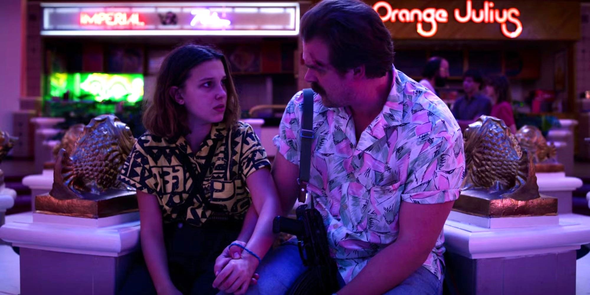Hopper sits next to Eleven and they hold hands as they talk in the Starcourt mall in Stranger Things.