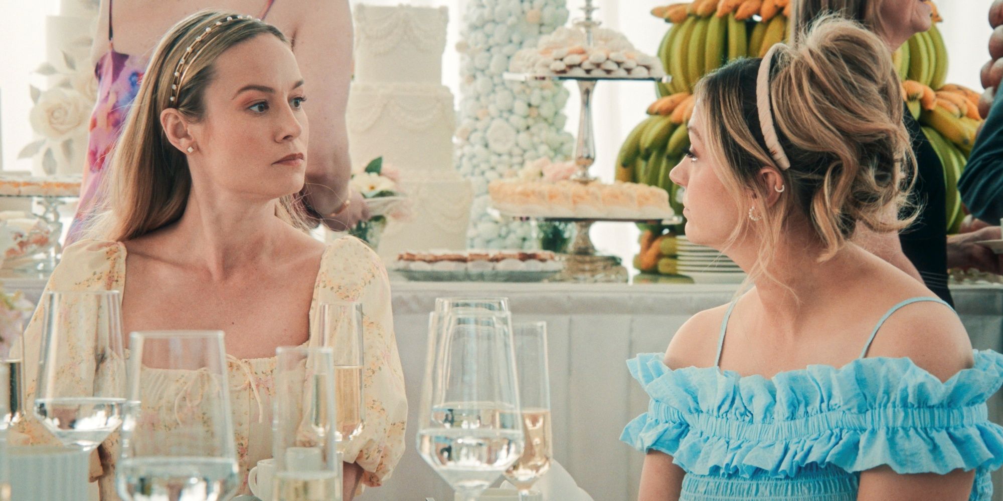 Abby Elliott as Sugar sitting at a table with Brie Larson as Francie at Tiff's wedding in Season 4 of The Bear.