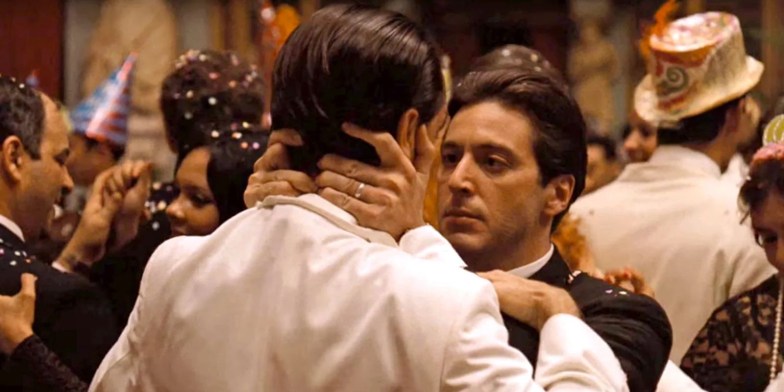 A man holds another man by the face at a party and stares at him intently in The Godfather Part II, 1974.