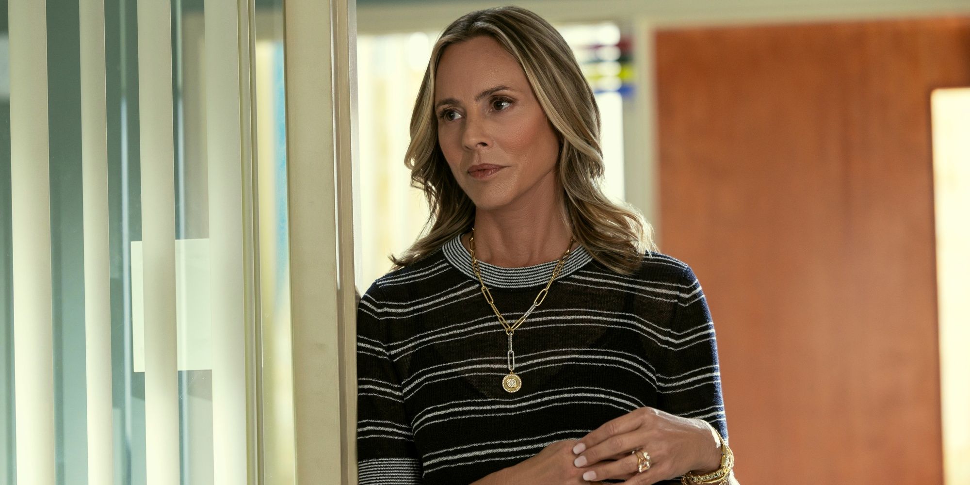 Maria Bello as Belle Buckley leaning her right shoulder against a wall while standing in The Waterfront