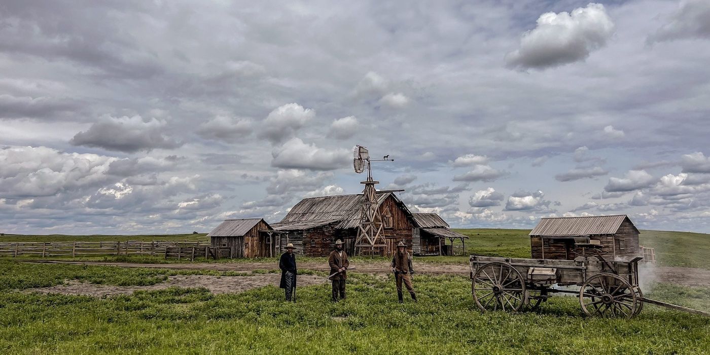 Three men stand in the field outside a rustic barn, with a big cloudy sky above them in Kevin Costner's The West.
