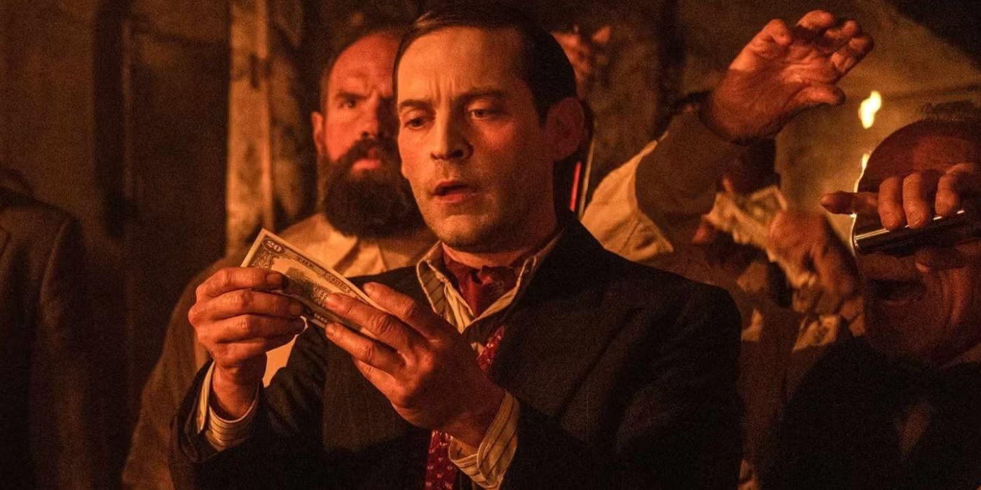 Tobey Maguire as James McKay looking earnestly at a bill of money with people behind him in Babylon.