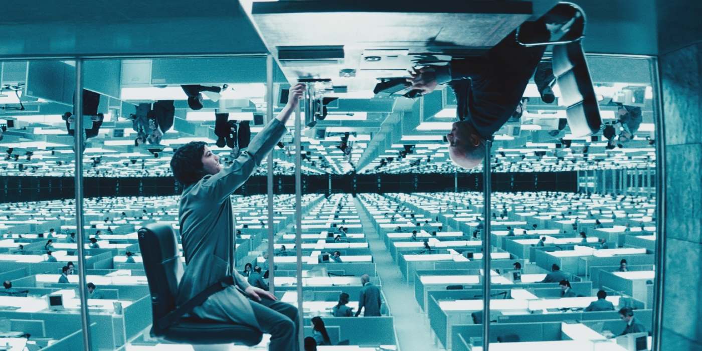 A man reaching for another man who's working on a desk on the ceiling in Upside Down