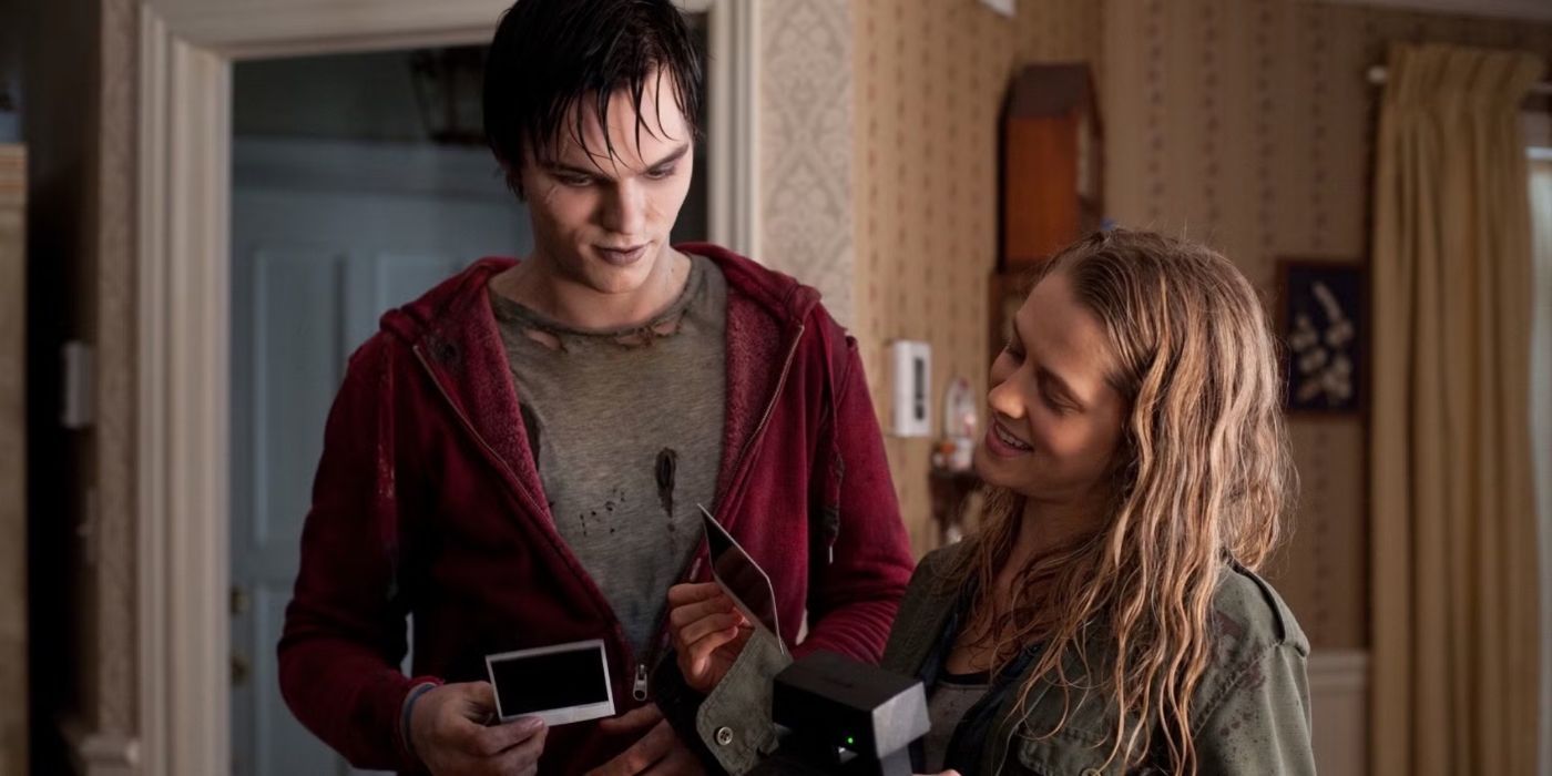 Nicholas Hoult and Teresa Palmer stand together in a house, looking at polaroids in 'Warm Bodies'.