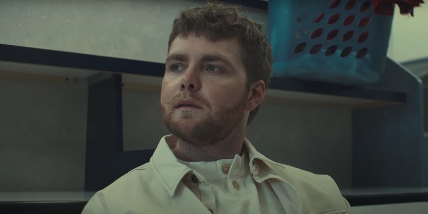 Alex Warren, sentado e olhando para alguém, em seu videoclipe para "Ordinário."