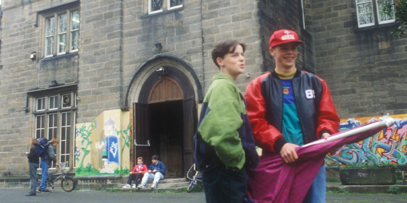 Two young people look to the distance and talk on a city street in Byker Grove.