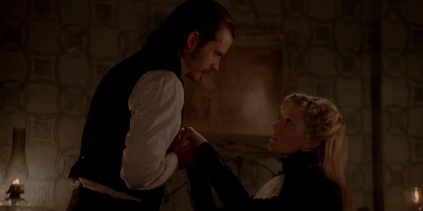 Seth standing and holding Martha's hand and talking down to her while she sits, looking up at him