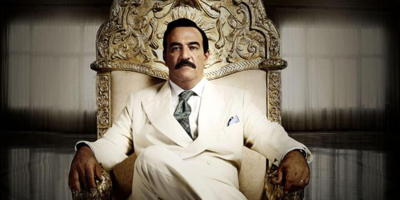 A man in a suit and mustache sits on an ornate chair and faces the camera in House of Saddam.