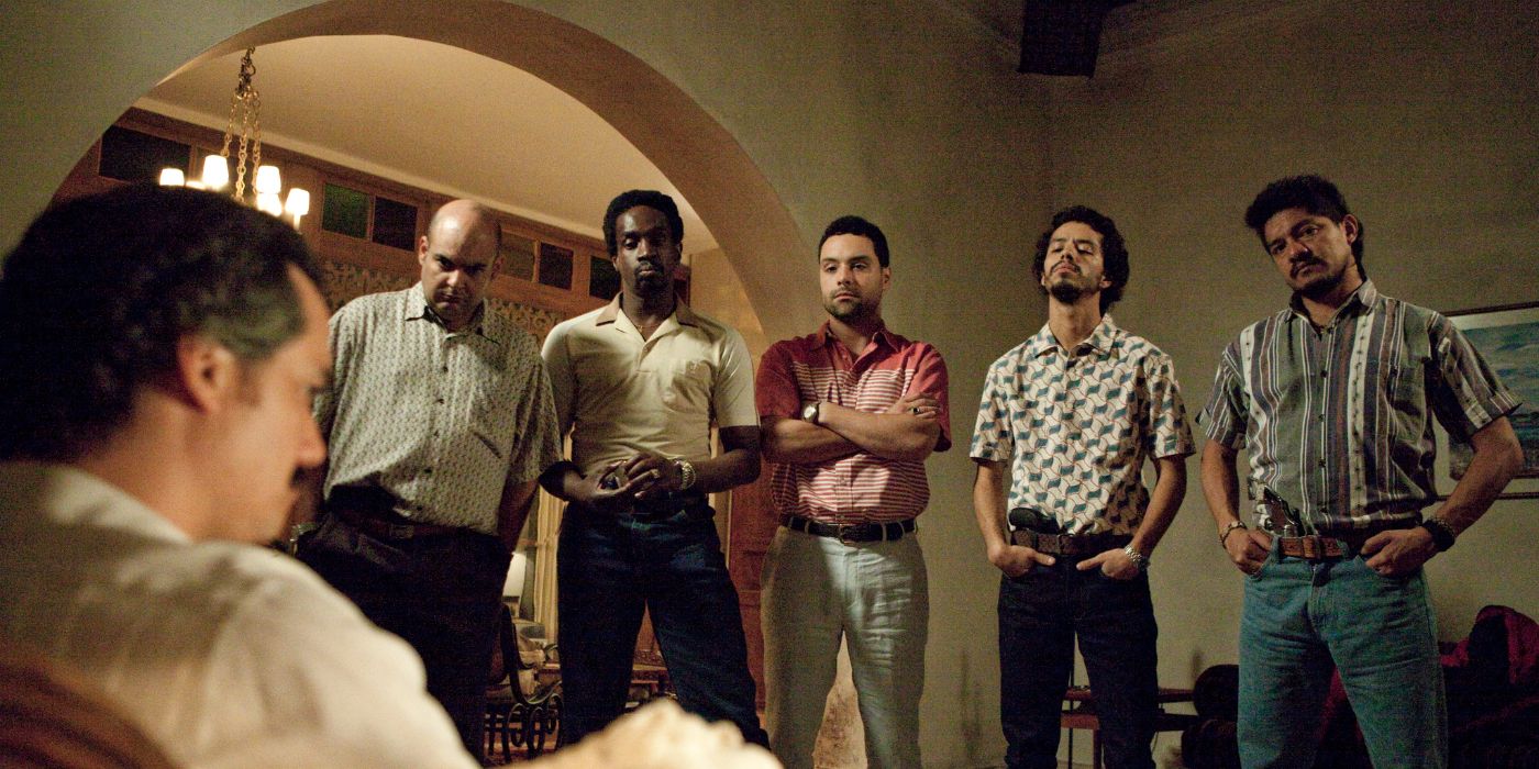Wagner Moura sitting in a chair looking at his soldiers who are lined up and looking at him in Narcos, "Los Pepes"